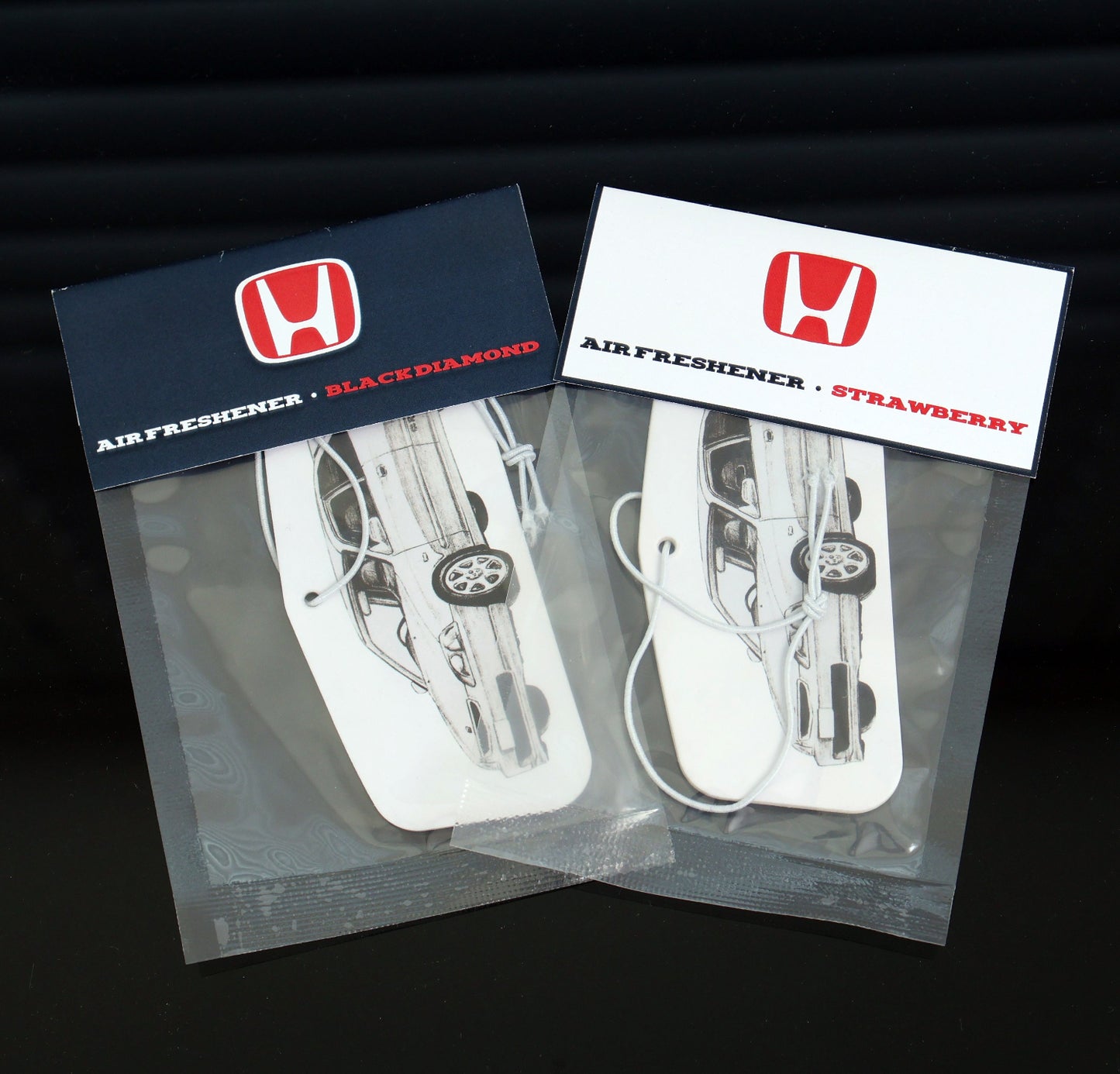 Honda EK Civis air freshener card available in Black Ice and Strawberry scents. Measures: H: 4.5cm, W: 10cm. Each air freshener comes sealed and each includes an elastic tie.