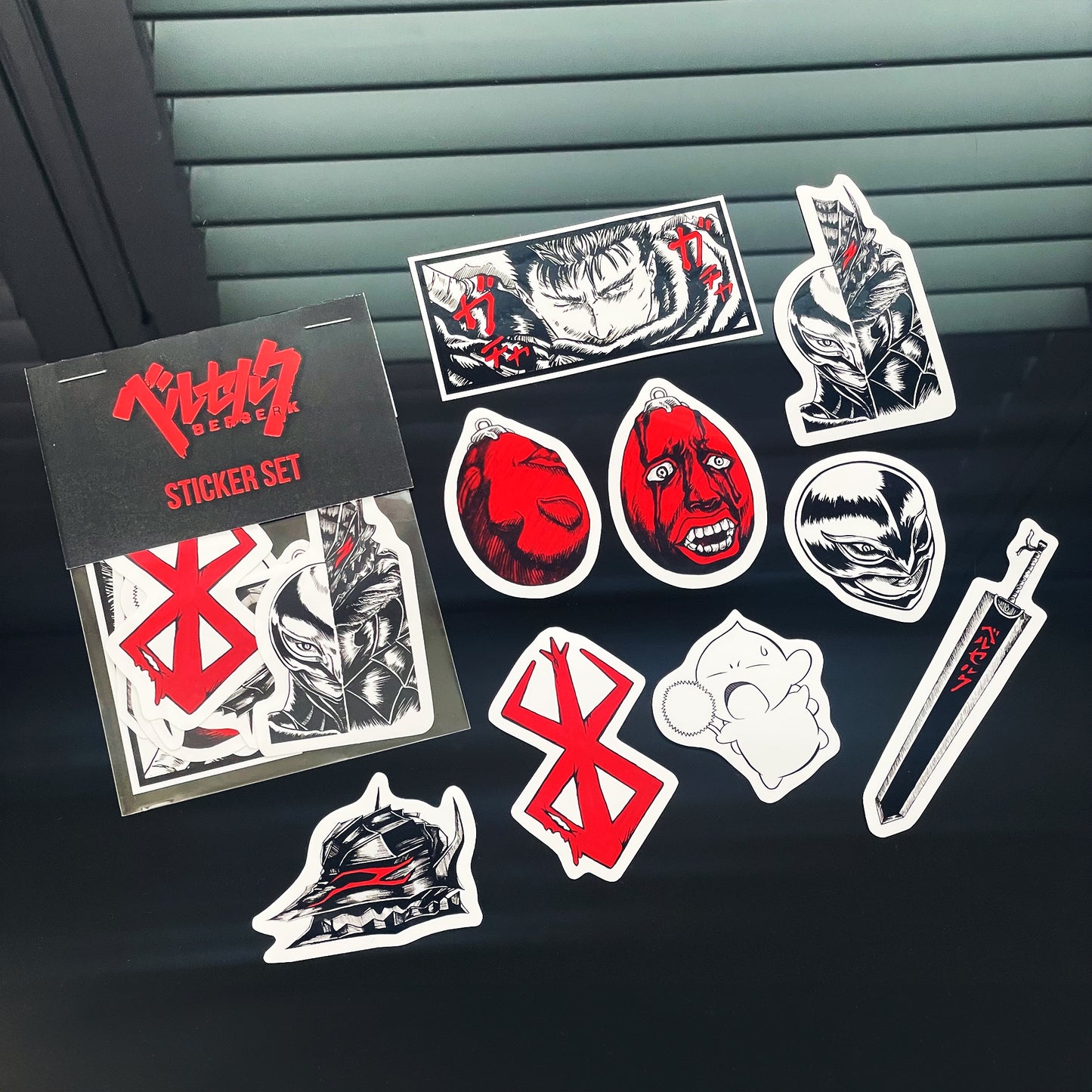 Berserk Sticker Pack showing details of 9 original designs stickers: Guts panel, Guts v. Griffith design, Brand of Sacrifice, Dragon Slayer sword, Behelit x2, Guts helmet, Chestnut Puck, and Femto Griffith helmet.