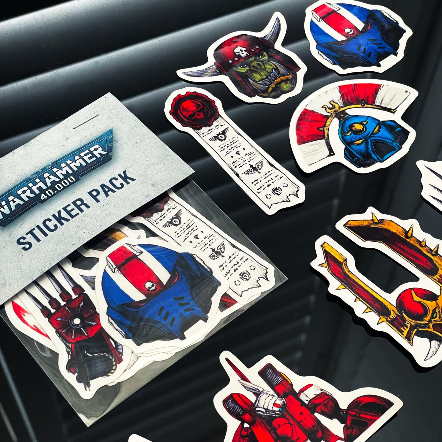 Closeup of Warhammer 40,000 sticker pack with various themed stickers on a dark surface.