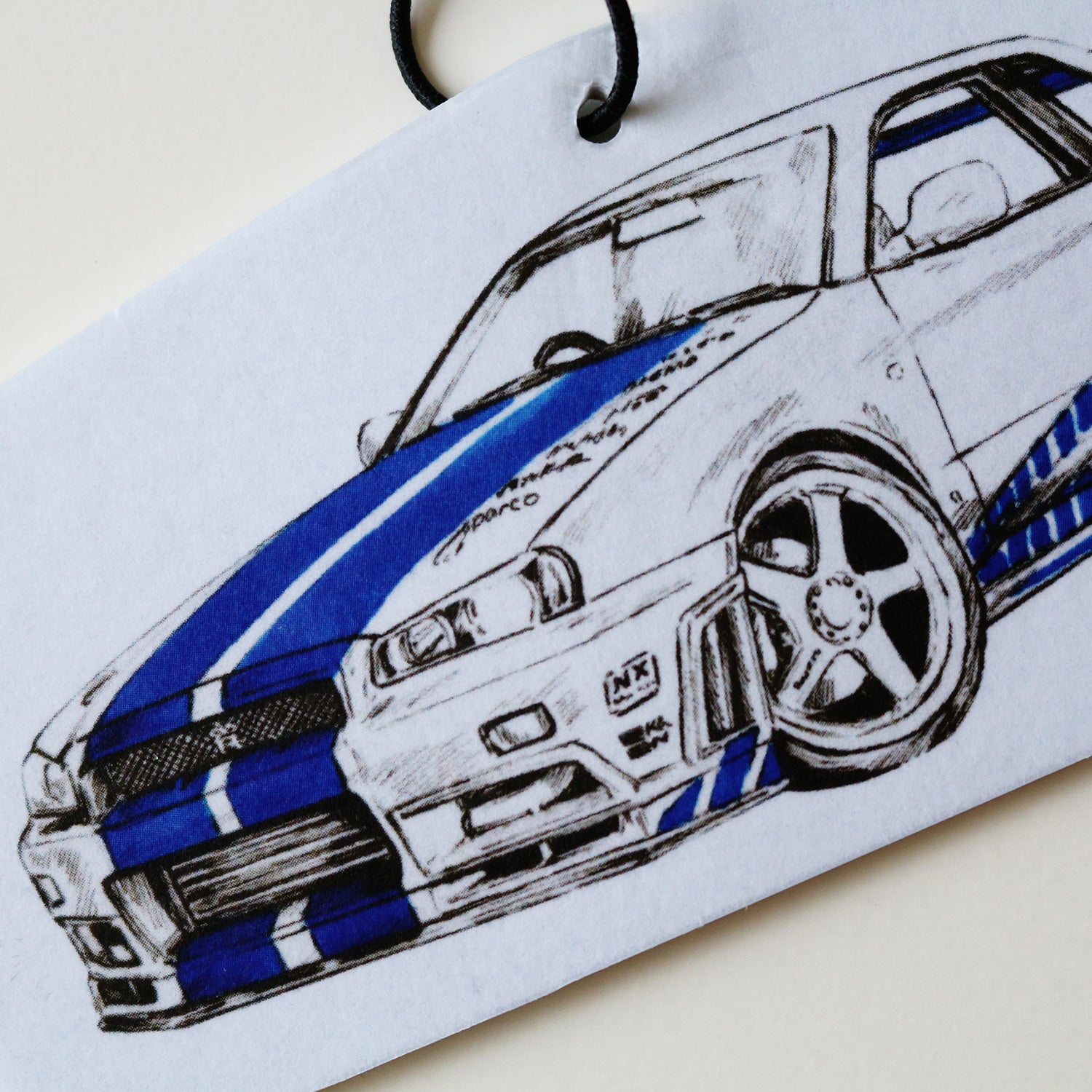 Close‑up of Brian’s R34 GT‑R air freshener showing front detailed blue Skyline artwork.