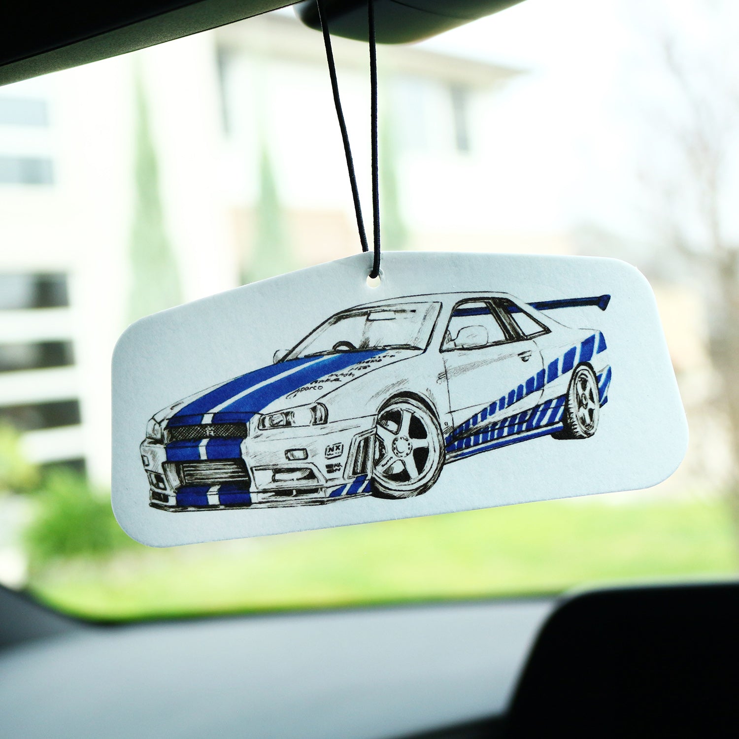 Blue R34 GT‑R car air freshener with illustrated Skyline design, JDM‑style artwork hanging card, displayed in vehicle cabin.