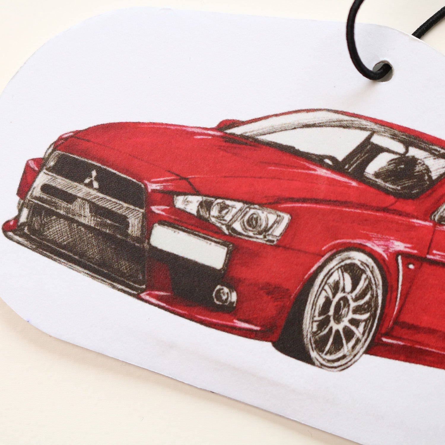 Close‑up of red body and front end of Mitsubishi Lancer EVO X air freshener showing detailed hand‑drawn artwork.