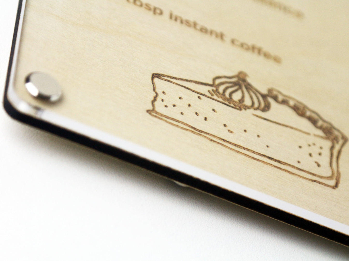 A bottom corner close-up of a custom engraved Recipe LayaBoard with acrylic dry‑erase surface for displaying family recipes.