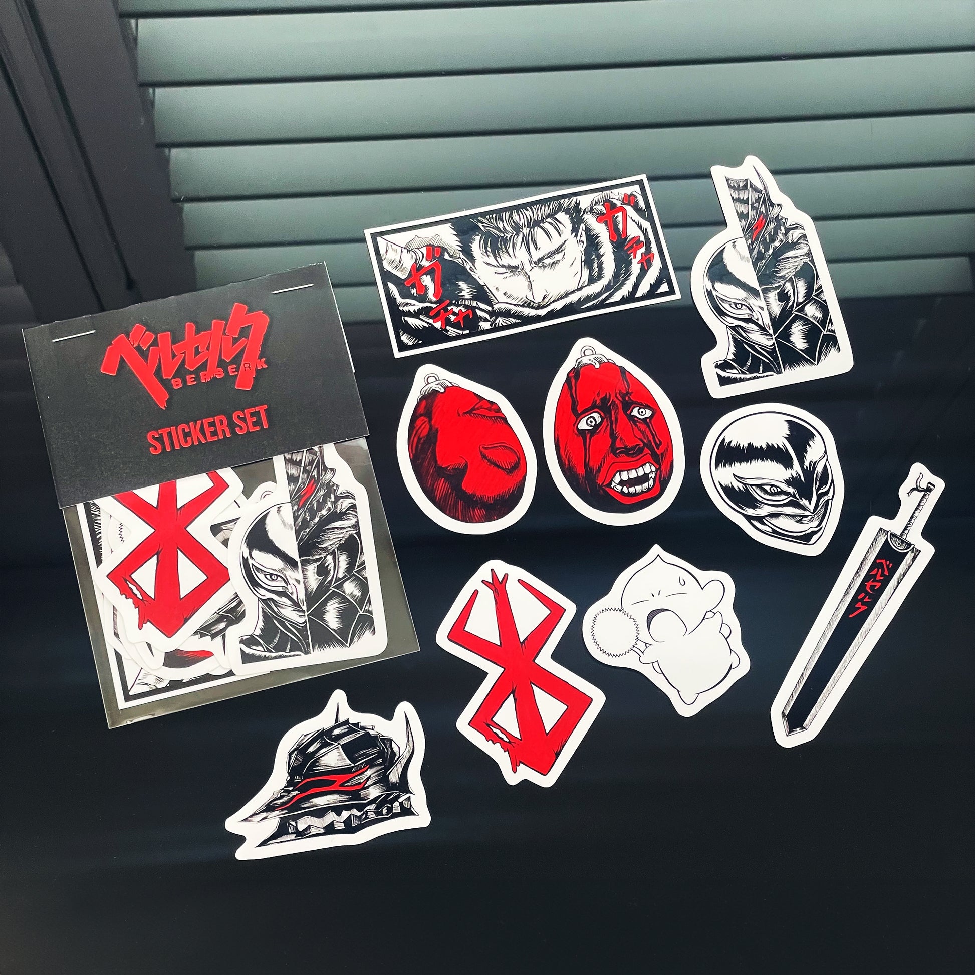 Berserk Sticker Pack showing details of 9 original designs stickers: Guts panel, Guts v. Griffith design, Brand of Sacrifice, Dragon Slayer sword, Behelit x2, Guts helmet, Chestnut Puck, and Femto Griffith helmet.