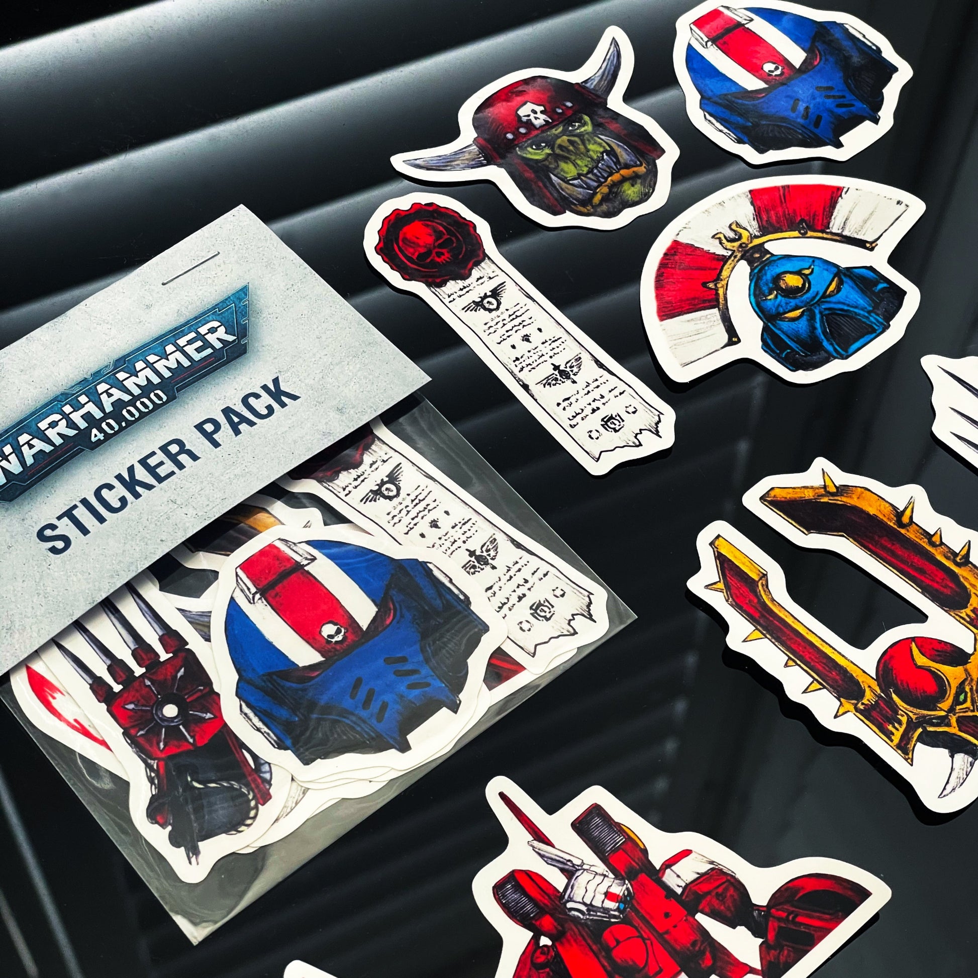 Closeup of Warhammer 40,000 sticker pack with various themed stickers on a dark surface.