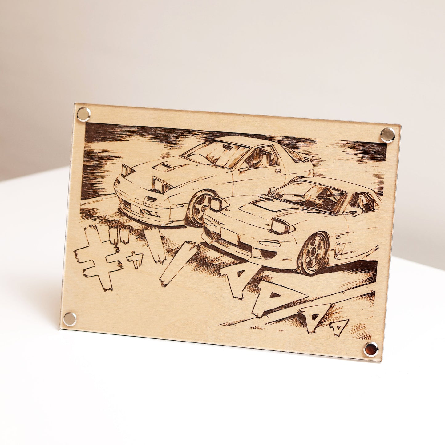 Laser-engraved artwork displayed on table featuring iconic Mazda RX-7 FC3S and FD3S with Japanese text inspired by Initial D.